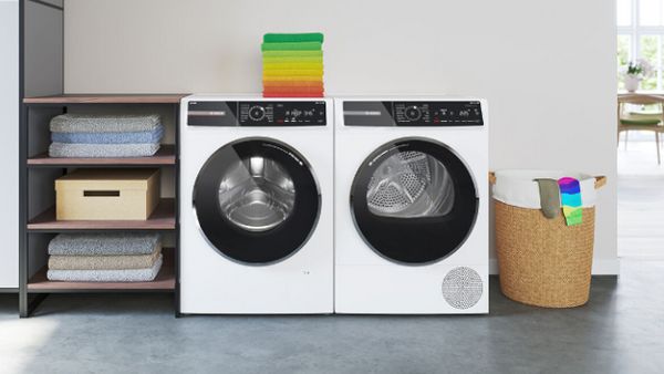 Dva pralna stroja, nameščena poleg kopalniškega umivalnika. Na vrhu levega pralnega stroja sta razporejeni dve zeleni brisači.