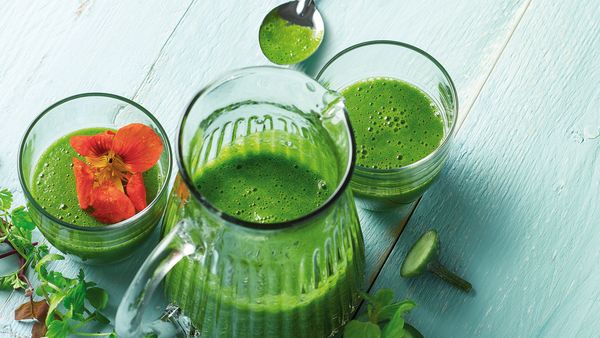 Green smoothies in glasses and edible flower garnish.