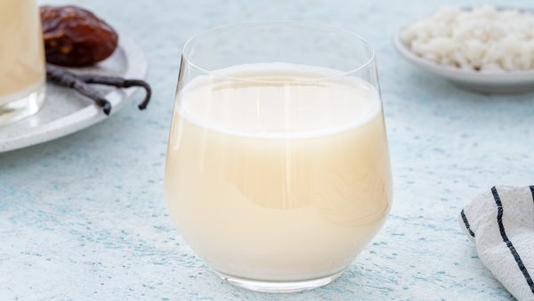 Mandelmælk i et glas ved siden af vaniljestænger og dadler.