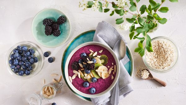 Purple smoothie bowl with various toppings and separate small bowls containing berries, pine nuts and seeds.