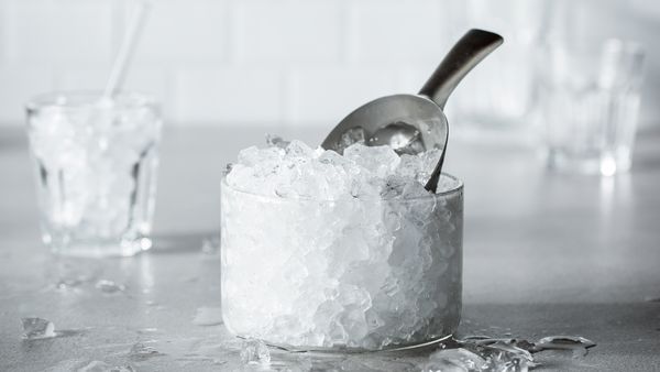 Bucăţi de gheaţă într-un recipient din sticlă cu o cupă, lângă un pahar plin cu gheaţă.