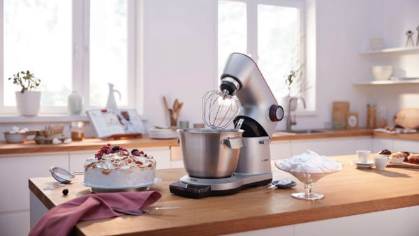 Robot de cocina Bosch con un batidor al lado de un pastel y crema batida.