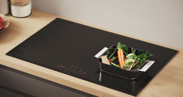Bosch Serie 6 inductiekookplaat met een pan met groenten en een wortel met zonnebril.