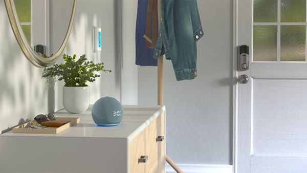 Foto van een hal naar de voordeur, aan de zijkant een dressoir met een smart speaker. In de hoek staat een kapstok met netjes opgehangen jassen.