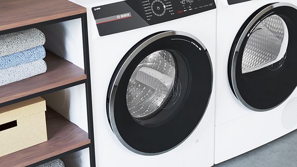 To vaskemaskiner placeret ved siden af hylder med håndklæder. Der står en potteplante oven på den venstre maskine.
