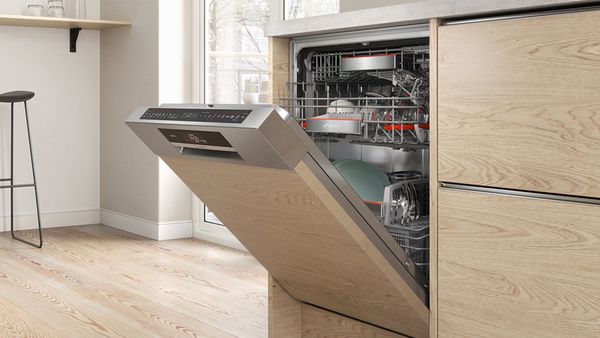 Uma máquina de lavar loiça aberta cheia de loiça limpa, perfeitamente integrada numa cozinha com painéis de madeira.