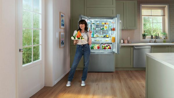 Réfrigérateur Bosch ouvert avec une femme tenant une montagne de légumes