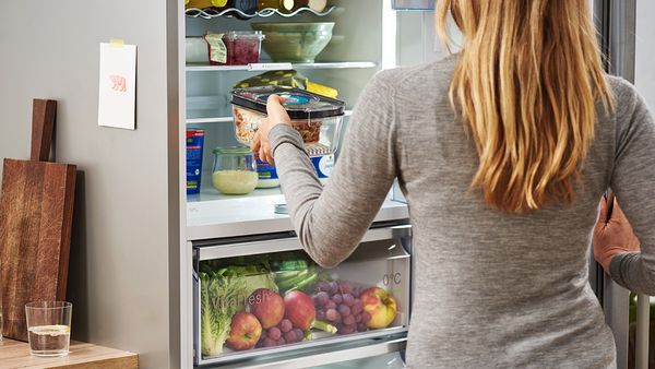 A woman placing packaged leftovers in a refrigerator.