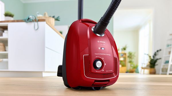 A red vacuum cleaner made of recycled plastic sitting on the floor of a bright and modern kitchen.