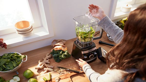 Person adding ice cubes to a Bosch blender to make a green smoothie.