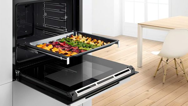 Open oven with a removable tray filled with cooked vegetables. 