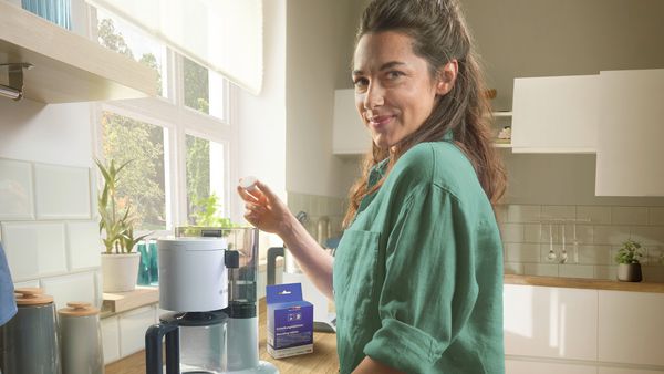 In a kitchen, a girl is holding a descaling tablet for a coffee machine.