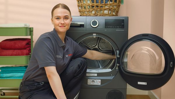 A Bosch technician is on her knees repairing a washing machine. 