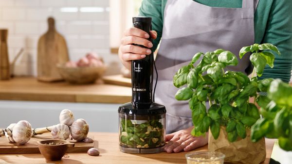 Eine Frau bereitet mit dem Bosch Stabmixer ErgoMaster mit Universalzerkleinerer frisches Pesto zu.