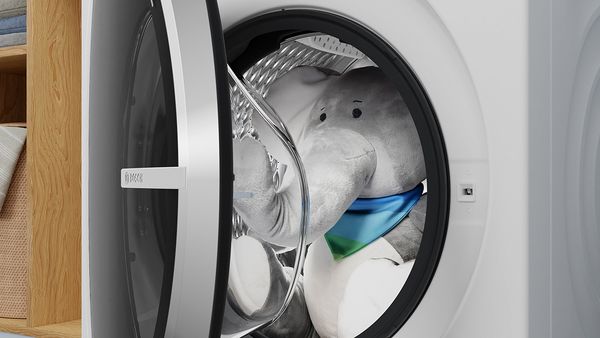Pohľad zblízka na práčku so sušičkou s čiastočne otvorenými dvierkami, ktoré odhaľujú vnútro bubna. Vnútri sa nachádza hračka slona, ktorá dodáva spotrebiču nádych roztomilosti.