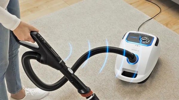 Blue lines indicating power emanate from a Bosch bagged vacuum that is being used to clean a rug.