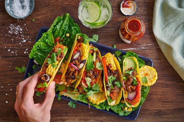 Tacos mit Salat, Jackfruit und Mais, angerichtet auf einem rechteckigen dunkelblauen Servierteller.
