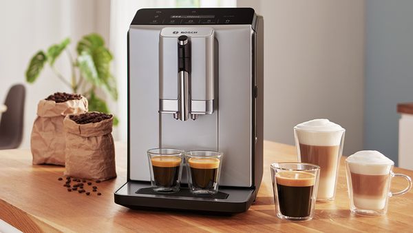 Serie 2 VeroCafe Kaffeevollautomat mit zwei Tassen Espresso auf der Tropfschale, daneben Latte Macchiato, Kaffee und Cappuccino auf einer Küchenarbeitsplatte.