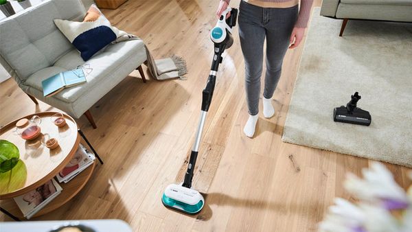 A person vacuuming and mopping a hard wood floor with a Bosch Unlimited 7 Aqua vacuum and mop