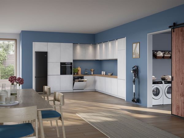 Eine moderne Küche, die Wand in gesetztem Blau; ein kabelloser BOSCH Staubsauger hängt an der Wand rechts. Daneben ein Raum mit Waschmaschine und Trockner,