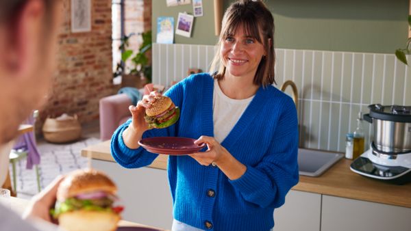 Eine Frau steht in der Küche und hält einen Burger über einem Teller in der Hand.