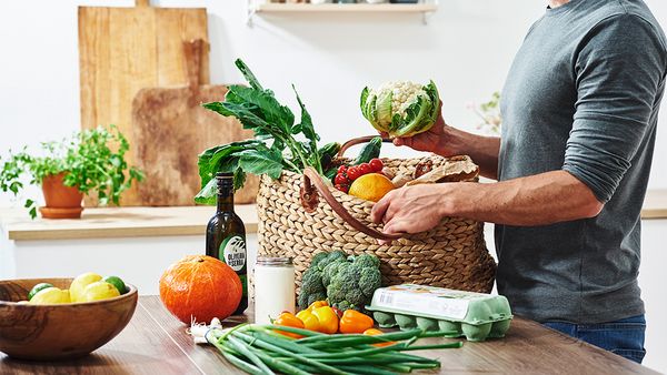 Eine Person packt eine Einkaufstasche mit frischem Obst und Gemüse aus.