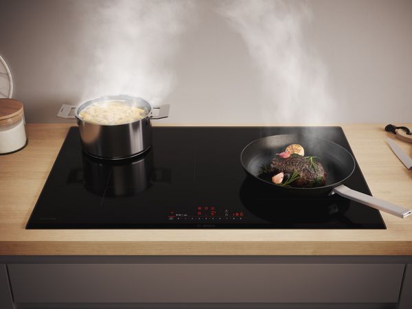 Een inductiekookplaat van Bosch met asperges en een biefstuk in de pan