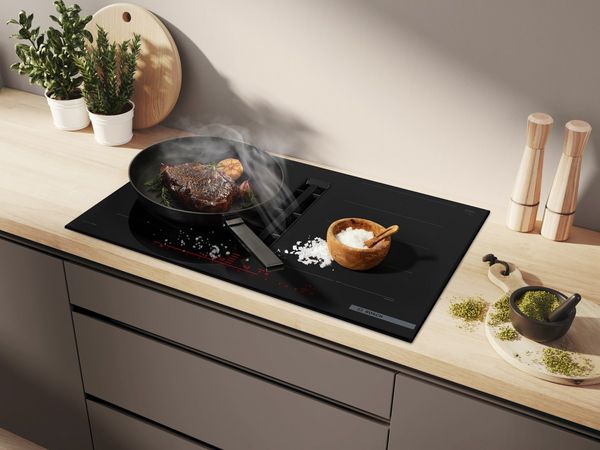 Een kookplaat met geïntegreerde ventilatie met daarop pannen waarin eten kookt terwijl de stoom wordt afgezogen.