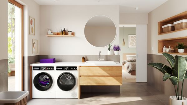 Zwei Waschmaschinen neben einem Waschtisch im Badezimmer. Auf der linken Waschmaschine befinden sich zwei grüne Handtücher.