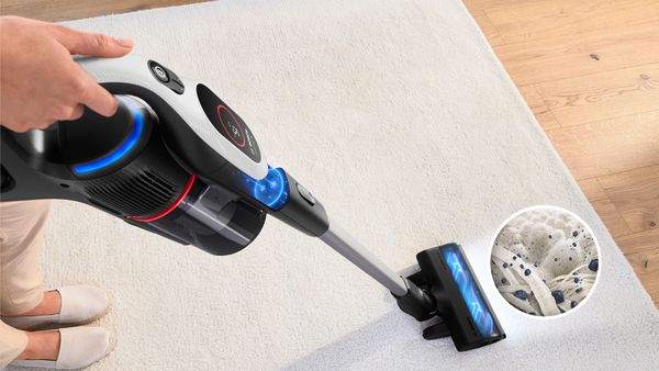 The Unlimited 9 vacuuming a carpet. A zoom shows microscopic particles being sucked in and detected by the MicroClean sensor.