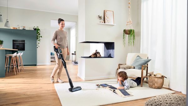 A woman and child are using an Unlimited 10 vacuum cleaner in a cozy living room, demonstrating teamwork in cleaning.