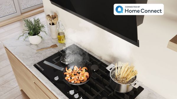 Un délicieux plat de pâtes est en train de cuire dans une casserole et la vapeur est extraite par la hotte inclinée.