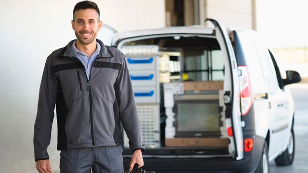 Technik serwisowy Bosch obok samochodu serwisowego z otwartymi tylnymi drzwiami, przez które widać znajdujące się w środku urządzenie.