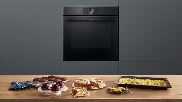 Serie 8 accent line ovn fra Bosch i et køkken. På bordpladen foran, er der forskellige bagværk som gulerodskage og muffins.