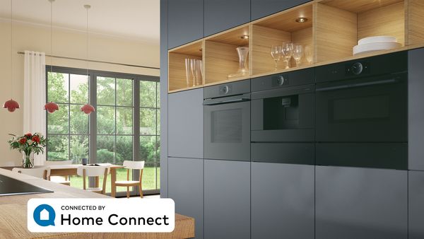 Elegant køkken med indbygningsovn i Serie 8 accent line og varmeskuffe. En tablet på bordet viser Bosch Home Connect Appen.