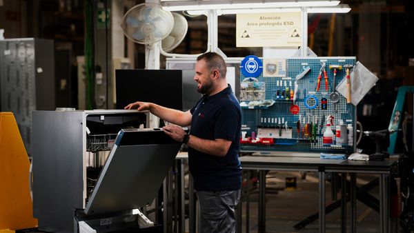 Technik Bosch sprawdzający zmywarkę w warsztacie, w tle widoczne narzędzia.