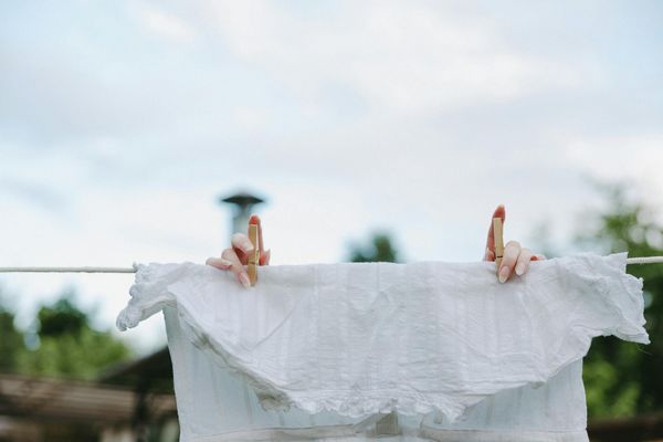 Osoba wiesza upraną białą bluzkę na sznurku do wysuszenia