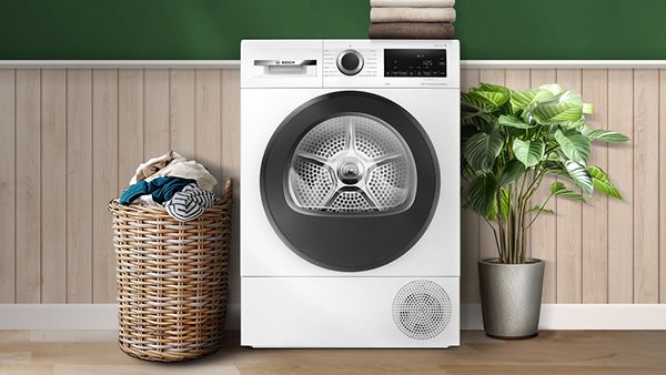 Bosch Heat Pump Tumble Dryer surrounded by clothes and a plant in wooden green room