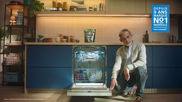 Un homme est accroupi à côté d'un lave-vaisselle ouvert rempli de vaisselle propre dans une cuisine moderne.