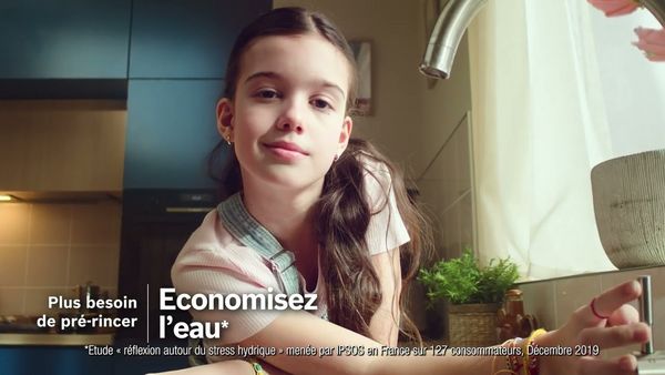 Un enfant dans une cuisine, faisant un geste vers un robinet, pour promouvoir la conservation de l'eau.