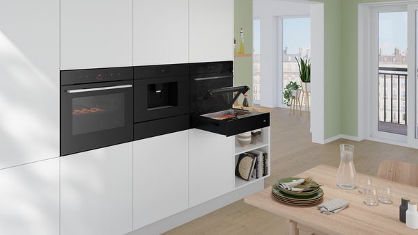 O bucătărie modernă cu un cuptor încorporabil, o plită şi un aparat de preparare cu aburi; un spaţiu luminos de luat masa în apropiere.