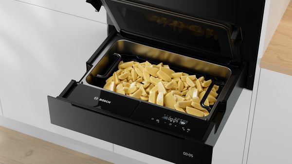 O bucătărie modernă cu un sertar termic Bosch deschis umplut cu cartofi tăiaţi cuburi.