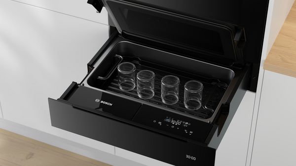 Un aparat Bosch cu un sertar deschis în care se pot vedea patru borcane din sticlă transparentă.