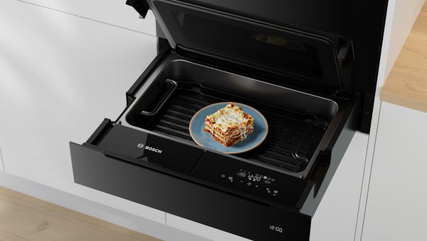 Într-un sertar al cuptorului Bosch se vede o porţie lasagna, iar în fundal se observă un mobilier de bucătărie modern.