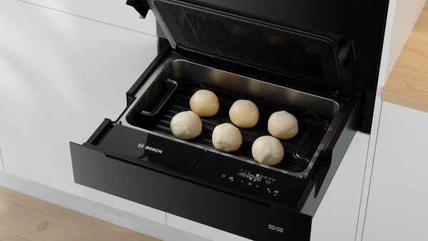 Un cuptor cu aburi Bosch în care este introdusă o tavă pentru grill pe care sunt aşezate şase bile rotunde de aluat.