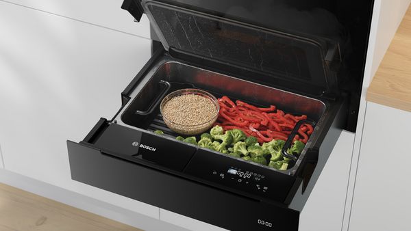 Un cuptor cu aburi Bosch plin cu broccoli, ardei graşi roşii şi un castron cu cereale, toate preparate cu aburi.