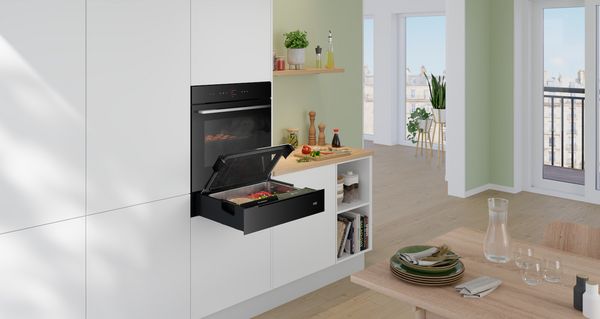 O bucătărie modernă cu dulapuri de culoare deschisă şi un cuptor elegant în case se află o tavă cu legume.