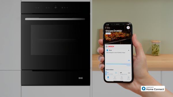 O persoană ţine în mână un smartphone, iar în fundal se vede un sertar de preparare cu aburi Bosch deschis.