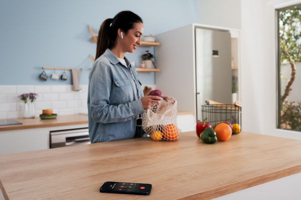 En kvinna packar upp matvaror i köket samtidigt som hon pratar med Bosch kundtjänst via sin smartphone.