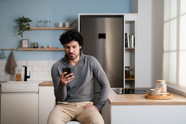 En mann bruker smarttelefonen sin på et moderne kjøkken foran et Bosch-kjøleskap.